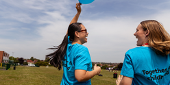 Two women in GOSH Charity t-shirts smile and walk through park holding GOSH Charity balloon