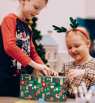 Girl with reindeer antlers hairband and a boy open a Christmas gift