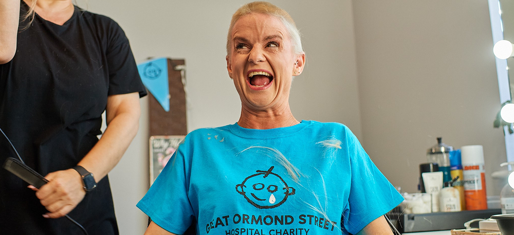 Woman sitting in hair salon chair, smiling. She has a shaved head.