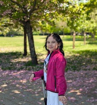 Girl standing on scooter in park, smiling.