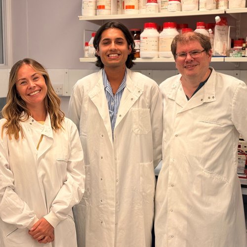 The research team behind the breakthrough stand in a lab, smiling to camera.