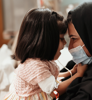 Little girl sits on her mum's lap, smiling.