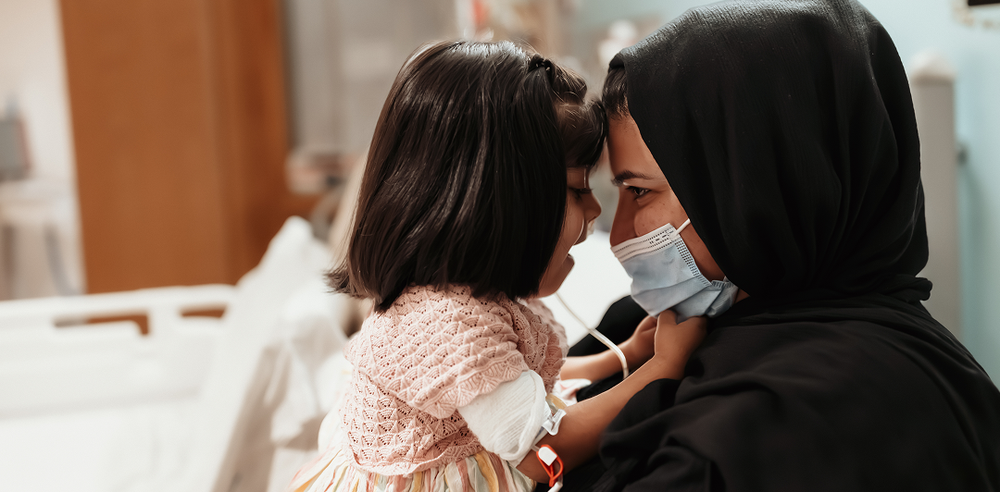 Little girl sits on her mum's lap, smiling.