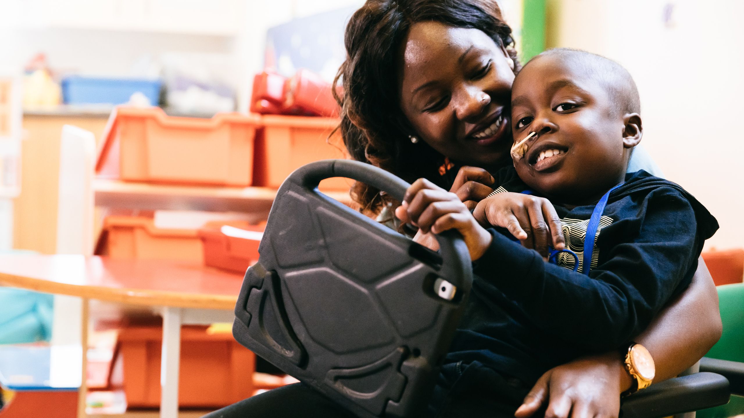 A young boy sitting on his mum's lap holds an iPad.