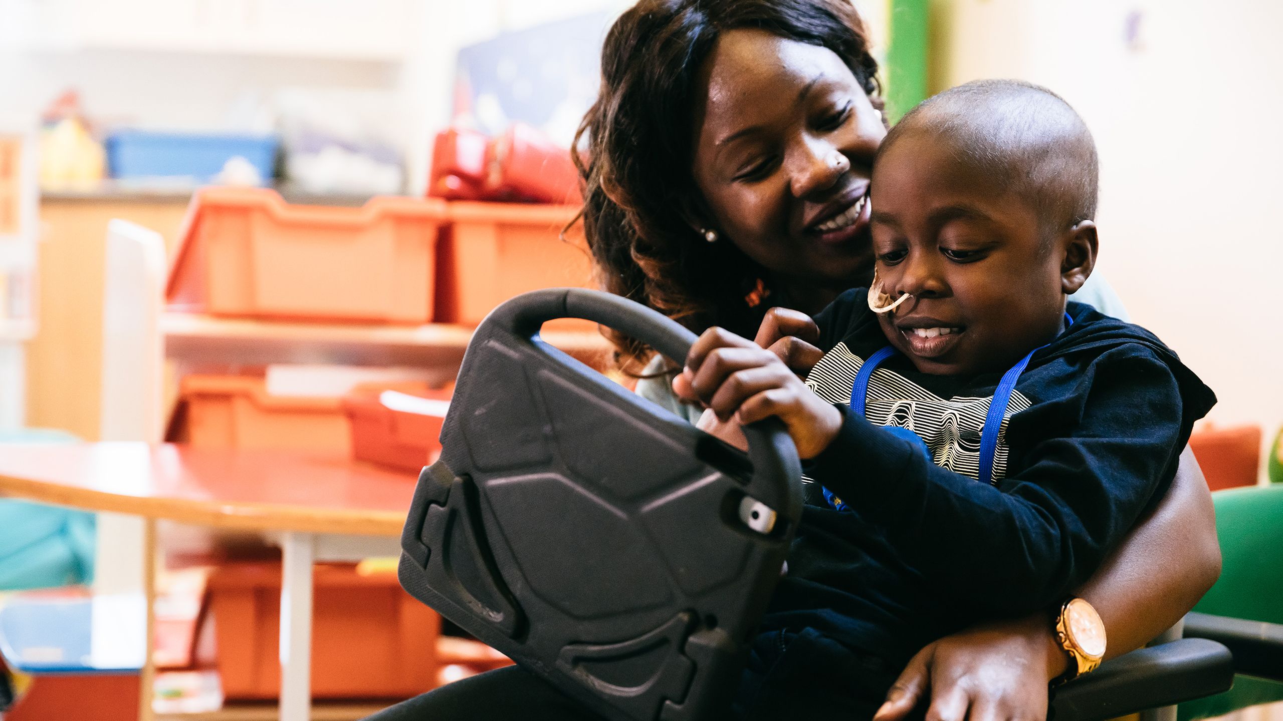 A young boy sitting on his mum's lap holds an iPad.