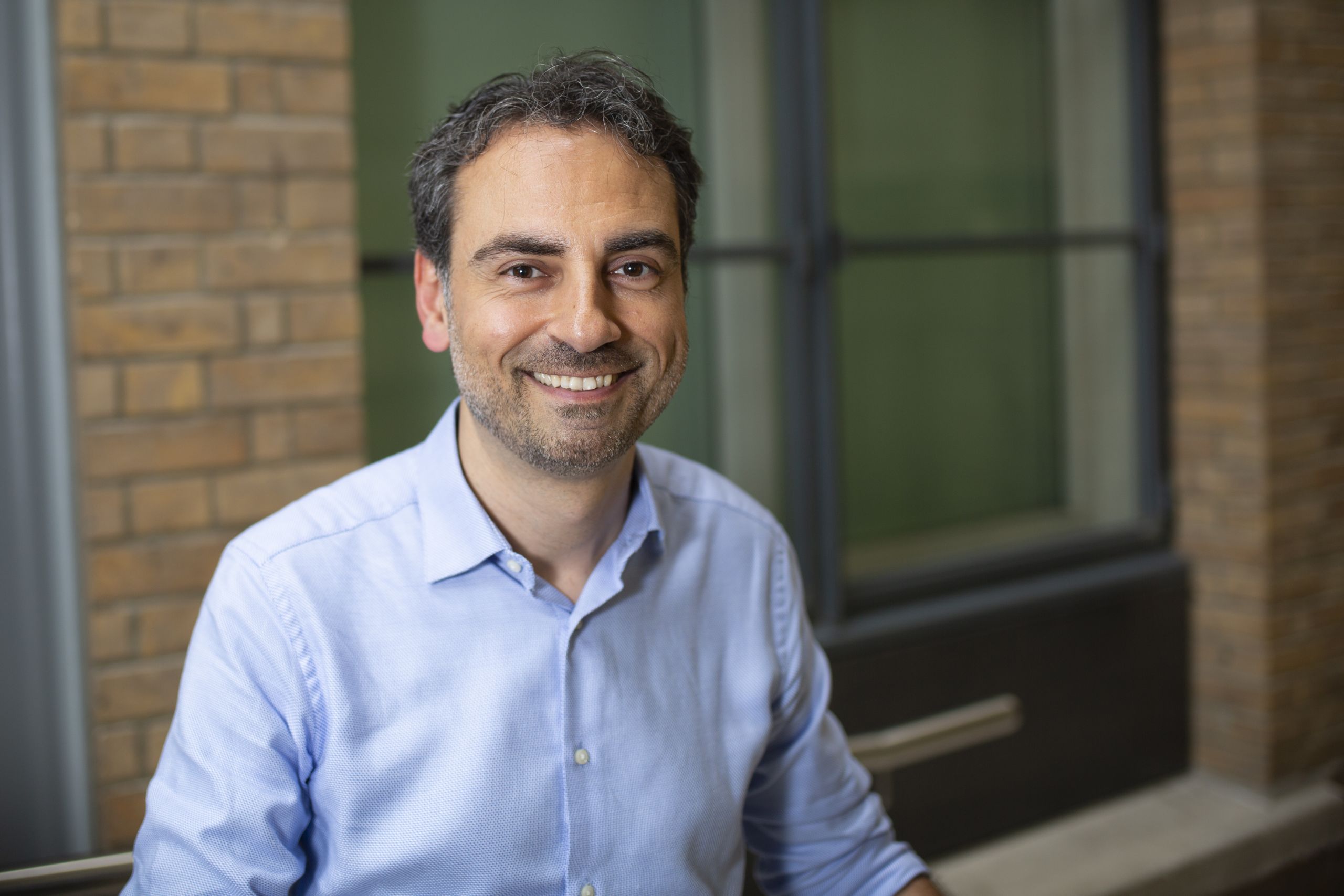 Dr Giovanni Baranello wears a blue shirt and smiles at the camera.